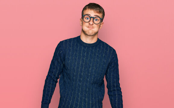 Young blond man wearing casual clothes and glasses puffing cheeks with funny face. mouth inflated with air, crazy expression.