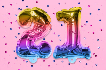 Rainbow foil balloon number, digit twenty one on a pink background with sequins. Birthday greeting card with inscription 21. Top view. Numerical digit. Celebration event, template.