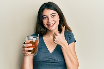 Young caucasian woman holding cup of tea smiling happy and positive, thumb up doing excellent and approval sign