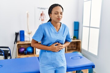 Young african american woman working at pain recovery clinic with hand on stomach because nausea, painful disease feeling unwell. ache concept.