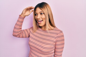 Fototapeta premium Beautiful hispanic woman wearing casual striped sweater very happy and smiling looking far away with hand over head. searching concept.