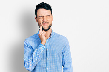 Hispanic man with beard wearing casual business shirt touching mouth with hand with painful expression because of toothache or dental illness on teeth. dentist