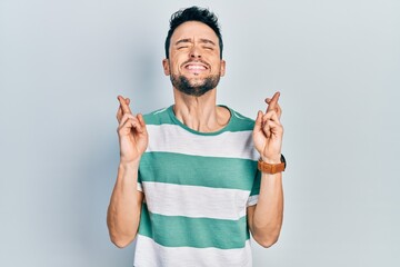 Young hispanic man wearing casual clothes gesturing finger crossed smiling with hope and eyes...