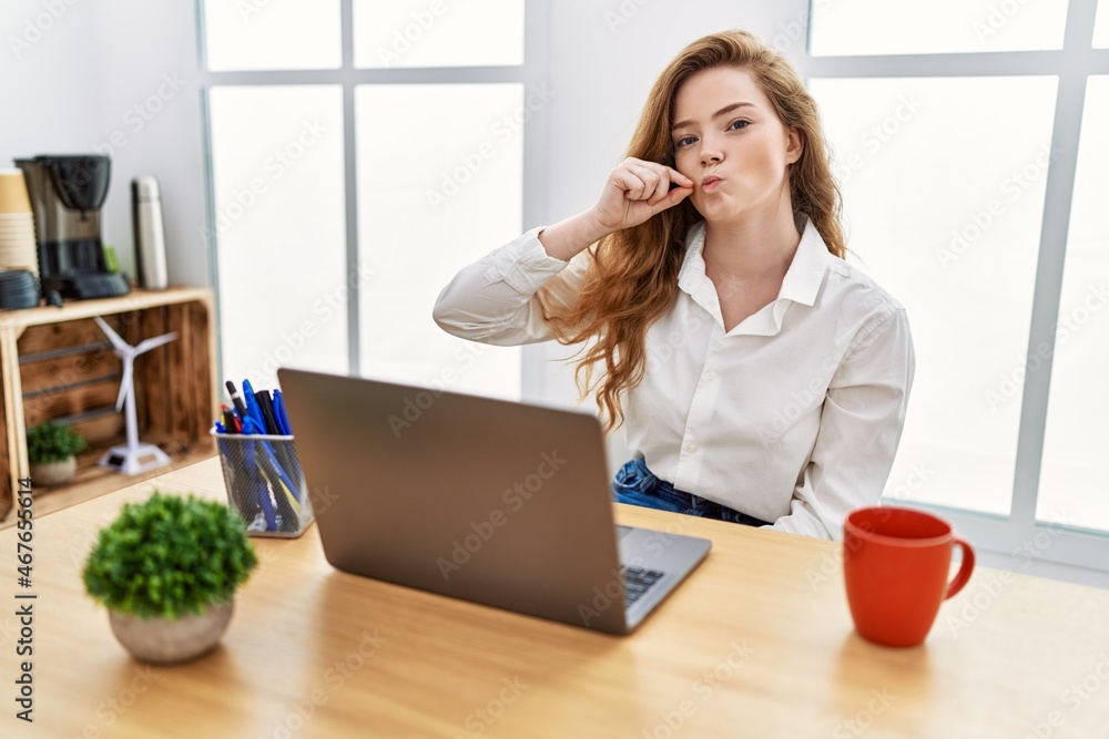 Poster young caucasian woman working at the office using computer laptop mouth and lips shut as zip with fi