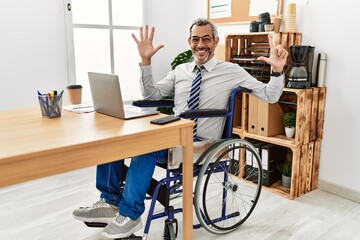 Middle age hispanic man working at the office sitting on wheelchair showing and pointing up with...