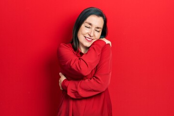 Middle age hispanic woman wearing casual clothes hugging oneself happy and positive, smiling confident. self love and self care