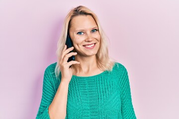Beautiful caucasian blonde woman having conversation talking on the smartphone looking positive and happy standing and smiling with a confident smile showing teeth