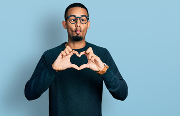 Young african american man doing heart symbol with hands making fish face with mouth and squinting eyes, crazy and comical.