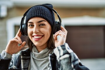 Young hispanic woman smiling happy using headphones at the city.