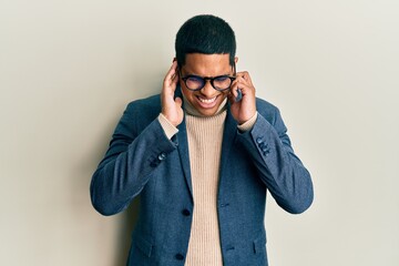 Obraz premium Young handsome hispanic man wearing elegant clothes and glasses covering ears with fingers with annoyed expression for the noise of loud music. deaf concept.