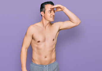 Fototapeta premium Handsome young man wearing swimwear shirtless very happy and smiling looking far away with hand over head. searching concept.