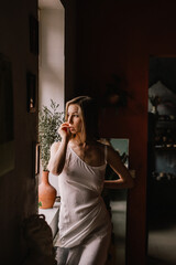 talented sculptor girl in light negligee stands in pottery workshop near large window. concept is beauty and art.