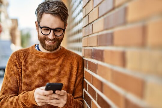 young caucasian man with beard  using smartphone outdoors on a sunny day