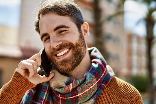 Caucasian man with beard having a conversation speaking on the phone outdoors on a sunny day