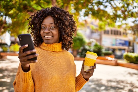 African american woman using smartphone drinking coffee at park