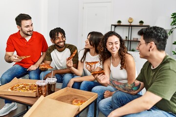 Group of young friends smiling happy eating italian pizza sitting on the sofa at home.