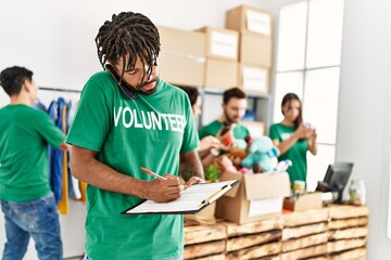 Group of young volunteers working at charity center. Man with serious expression writing on...
