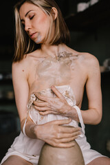 talented sculptor girl in thin light negligee sculpts a jug of clay in pottery workshop near large window. Concept art of sculpture