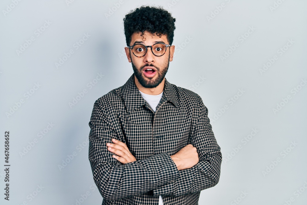 Sticker Young arab man with beard wearing glasses with arms crossed gesture afraid and shocked with surprise and amazed expression, fear and excited face.