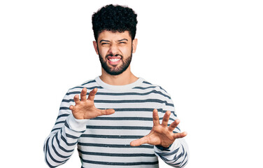 Young arab man with beard wearing casual striped sweater smiling funny doing claw gesture as cat,...