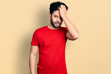 Young arab man with beard wearing casual red t shirt surprised with hand on head for mistake, remember error. forgot, bad memory concept.