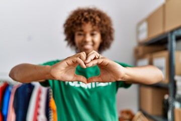 Young african american woman wearing volunteer uniform doing heart symbol with hands at charity center