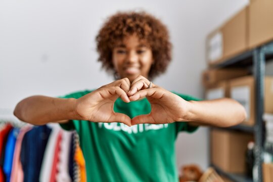 Young african american woman wearing volunteer uniform doing heart symbol with hands at charity center