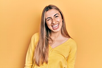 Beautiful hispanic woman wearing casual yellow sweater winking looking at the camera with sexy expression, cheerful and happy face.