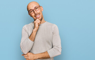 Bald man with beard wearing casual clothes and glasses looking confident at the camera with smile with crossed arms and hand raised on chin. thinking positive.