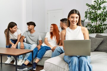 Fototapeta premium Group of young friends speaking sitting on the sofa. Woman smilimg happy and using laptop at home.