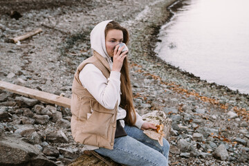 young woman drinking tea on river shore at autumn season
