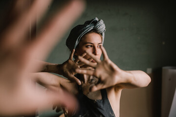 beautiful sculptor girl with a headband and a black apron shows her hands stained with clay. camera focus is on girl's face, blur is on her hands.