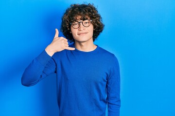 Handsome young man wearing casual clothes and glasses smiling doing phone gesture with hand and fingers like talking on the telephone. communicating concepts.