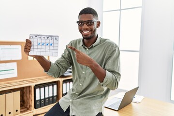 Young african american businessman holding travel calendar at the office smiling happy pointing with hand and finger
