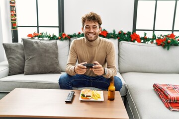 Young hispanic man playing video game sitting by christmas decor at home