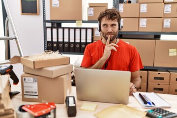 Young hispanic call center agent man working at warehouse thinking concentrated about doubt with finger on chin and looking up wondering