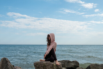 Meditating yoga. Tranquil woman. Nature harmony. Calm lady sitting Gomukasana pose on rock stone azure water blue sky view.