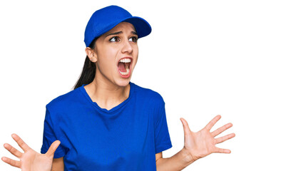 Young hispanic girl wearing delivery courier uniform crazy and mad shouting and yelling with aggressive expression and arms raised. frustration concept.