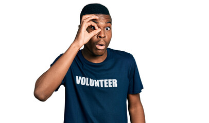 Young african american man wearing volunteer t shirt doing ok gesture shocked with surprised face, eye looking through fingers. unbelieving expression.