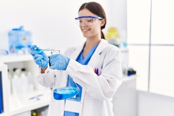 Fototapeta premium Young hispanic woman wearing scientist uniform holding test tube at laboratory