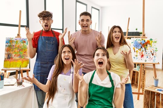 Group of five hispanic artists at art studio crazy and mad shouting and yelling with aggressive expression and arms raised. frustration concept.