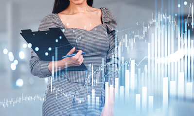 Businesswoman with clipboard, graph lines and candlesticks hologram, office room