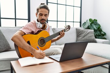 Handsome hispanic man practicing guitar with video tutorial at the living room at home