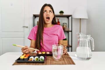 Obraz na płótnie Canvas Young brunette woman eating sushi using chopsticks angry and mad screaming frustrated and furious, shouting with anger. rage and aggressive concept.
