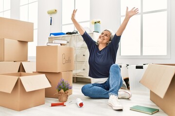 Middle age grey-haired woman smiling happy with hands raised up at new home.