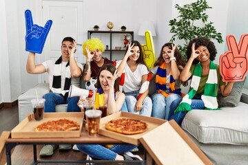 Group of young people wearing team scarf cheering football game smiling happy doing ok sign with hand on eye looking through fingers