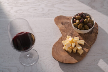 Red wine with olives and vintage cheese on white table