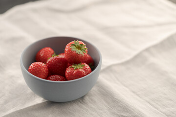 Organic ripe strawberries in blue ceramic bowl on white linen cloth