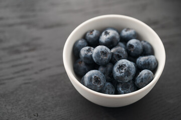 Organic ripe blueberries in white ceramic bowl on black oak table