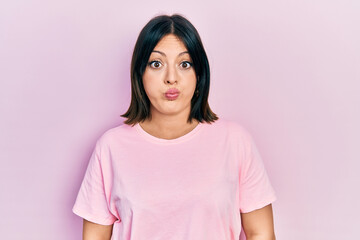 Young hispanic woman wearing casual pink t shirt puffing cheeks with funny face. mouth inflated with air, crazy expression.